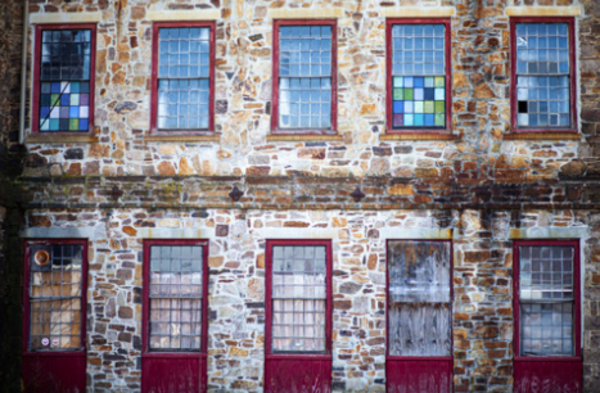 Color photograph of a wall of windows in an old mill building in Lawrence MA Brick wall The windows are many paned and some panes are blue purple or green