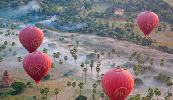 Four red hot air balloons seen from above over a foggy tree filled background Temple and home seen in distance 