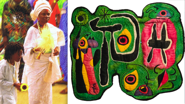 Photograph of Woman in white dress and headress holding yellow feather next to child with dreads wearing white and holding sunflower in front of colorfully dressed people out of focus next to quilted piece of textile art with green background and pink bl