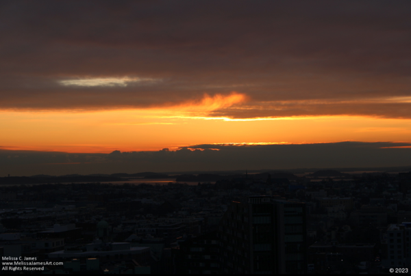 Sunrise in the distance. Orange sky with dark clouds in the upper portion 12 of the image. Land in darkness.