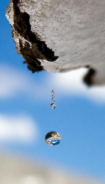 Drop of water falling off rocky ledge with blue sky in background 