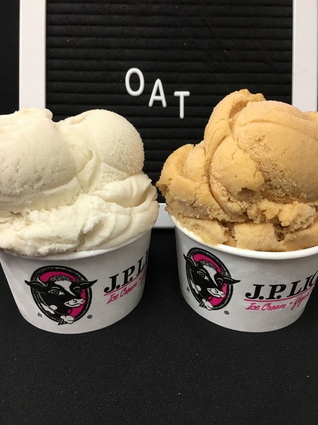 Vanilla Oat and Pumpkin Spice ice cream in two cups in front of a black sign with oat spelled out on it