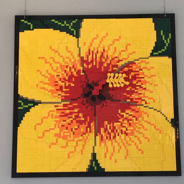 Yellow flower with red center made entirely of Lego Blocks in a square frame. 