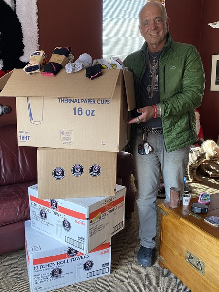 Man in green jacket gesturing toward stack of four cardboard boxes filled with socks 