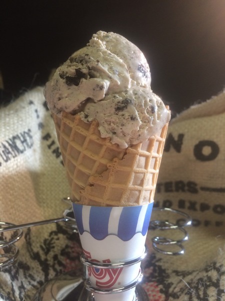 Salted Caramel Cookies n Cream ice cream in a waffle cone held in silver cone holder in front of burlap coffee bags 