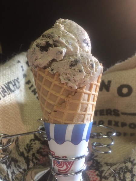 Salted Caramel Cookies n Cream ice cream in a waffle cone held in silver cone holder in front of burlap coffee bags. 